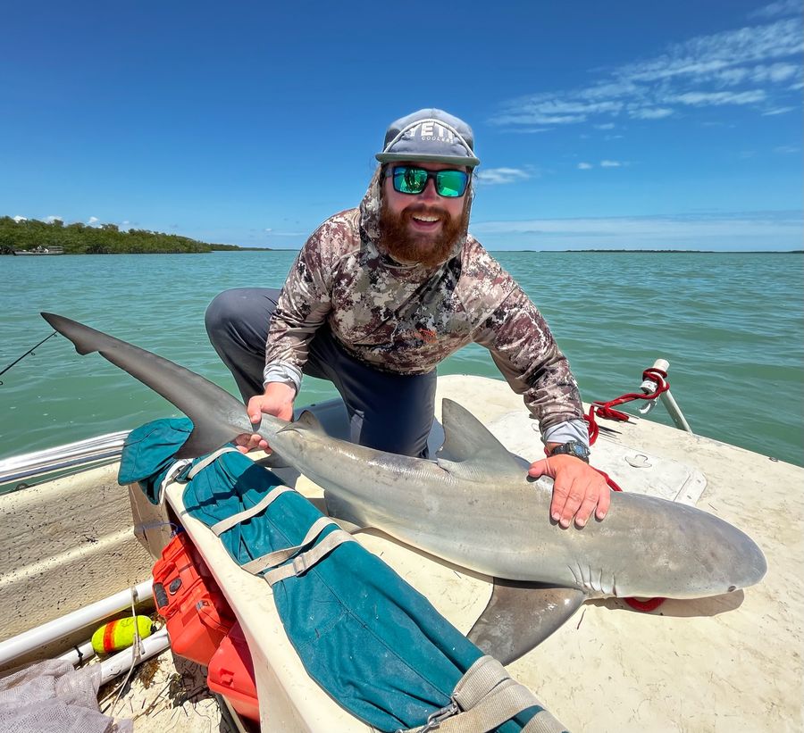 Mack kneeling on a boat with a shark