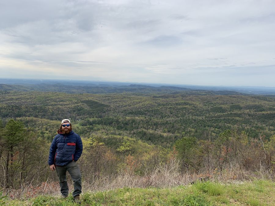 Standing on a grassy overlook above forested hills
