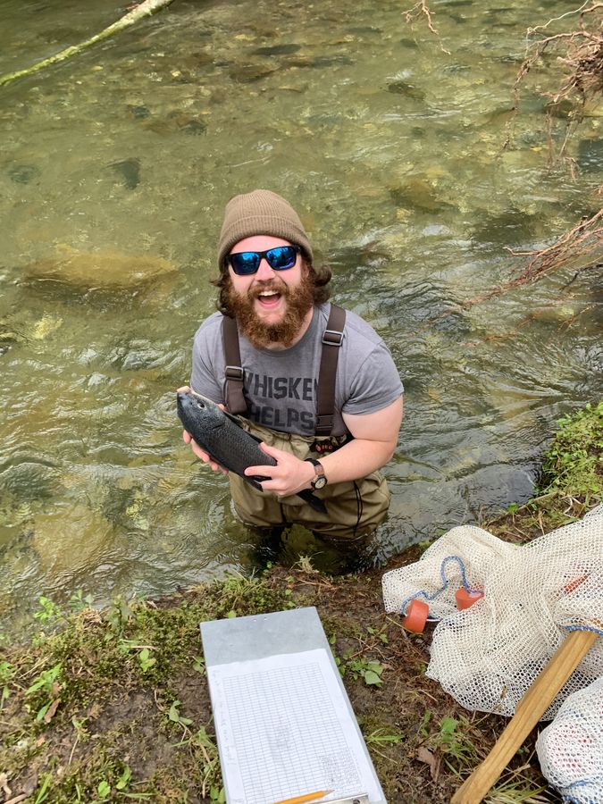 Mack standing in a stream holding a sucker